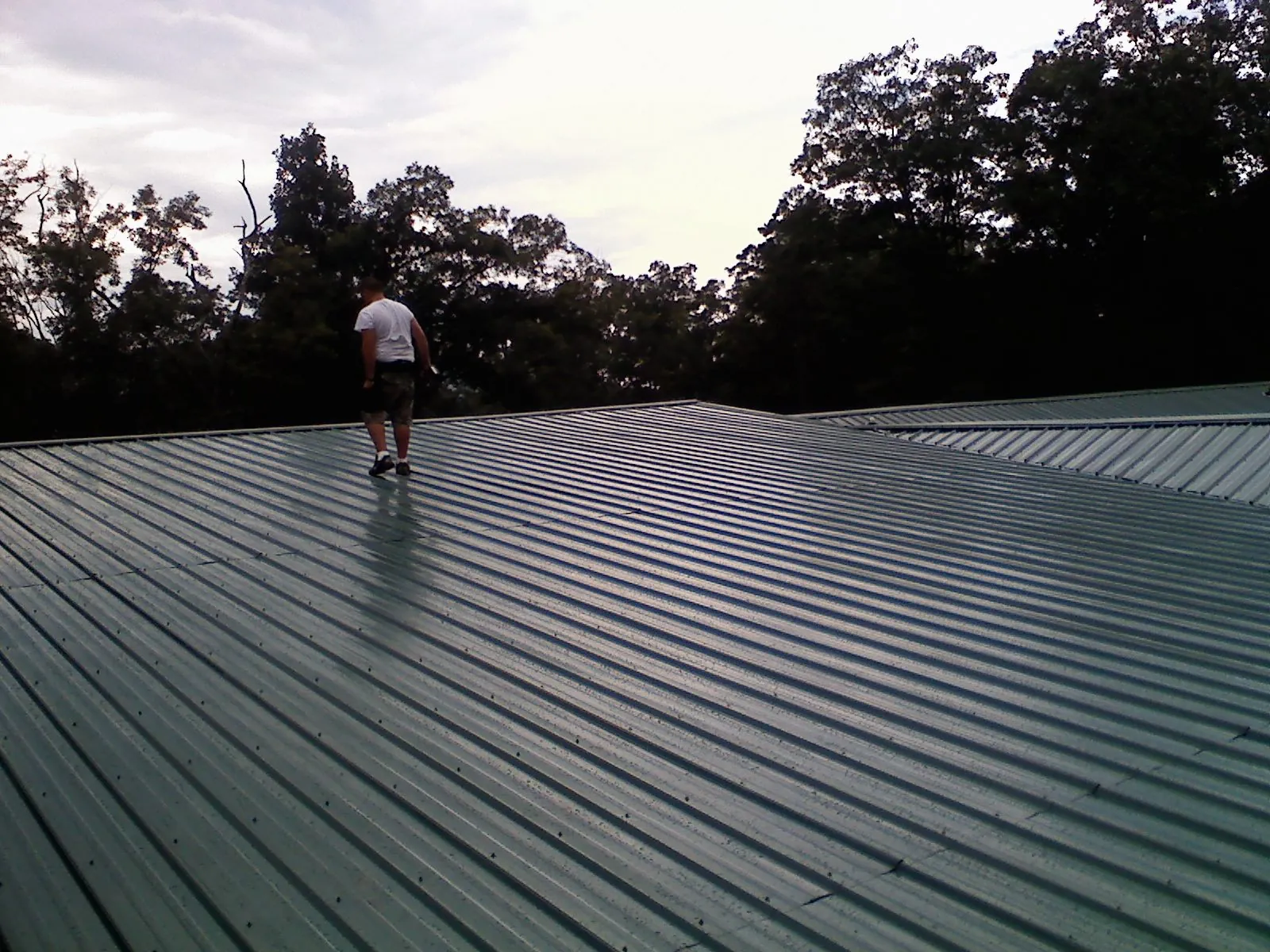 Roofer walking a wide expanse of new green metal roofing in Seymour